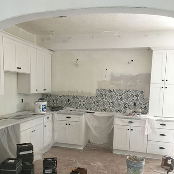 Renovation in progress: new kitchen cabinets and patterned tile backsplash with countertops under sheeting