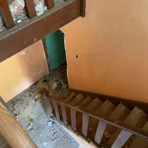 Work in progress: interior stairwell landing with plaster debris and a rough opening cut through the wall