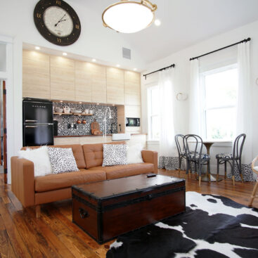 Open living area with tan leather sofa and wood floors beneath a vaulted ceiling with the kitchen wall behind
