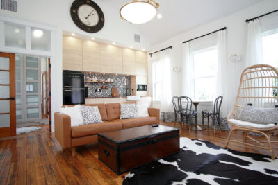 Open living area with tan leather sofa and wood floors beneath a vaulted ceiling with the kitchen wall behind