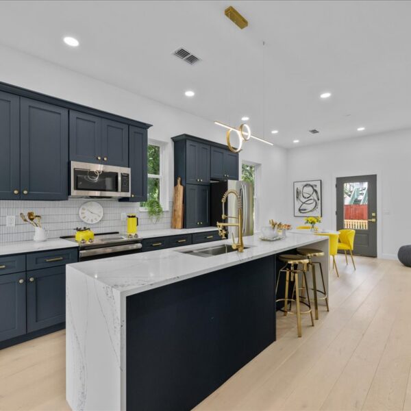 Open kitchen with navy cabinetry gold fixtures and a long veined white island facing the dining area