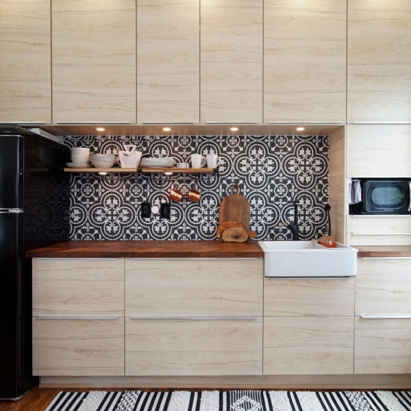 03-shotgun-house-kitchen-patterned-tile-backsplash Compact kitchen wall with pale wood cabinetry a patterned black and white tile backsplash and an apron sink