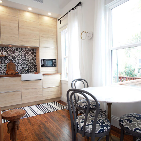 04-shotgun-house-kitchen-dining-nook-marble-table Round marble dining table and bentwood chairs sit beside tall windows just off the compact kitchen run