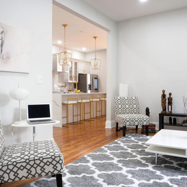 06-classic-colonial-living-room-open-to-kitchen Living room with patterned chairs framed by a wide cased opening into the kitchen beyond