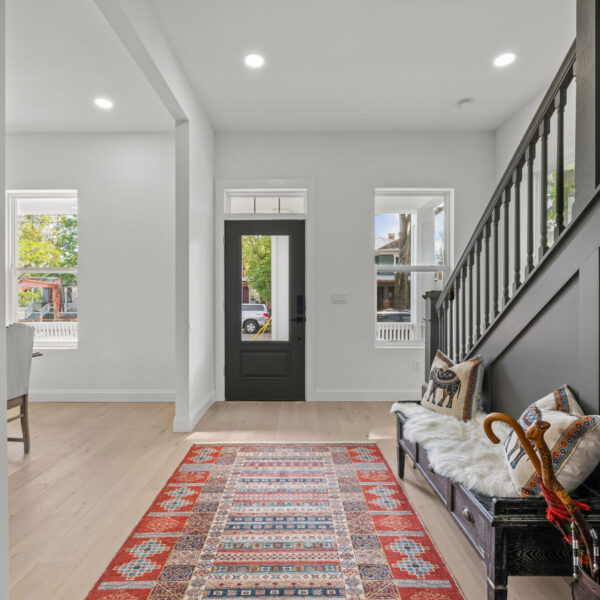 View toward the front door from the entry hall with a patterned runner and a bench along the stair wall