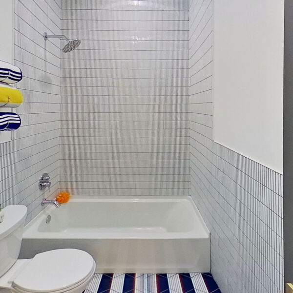11-magnolia-bathroom-tub-shower-white-tile-surround Bathroom with a tub and shower combination set into a white tile surround with striped floor tile