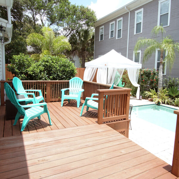 13-shotgun-house-deck-poolside-lounge-chairs Teal patio chairs line the raised deck beside the pool with a curtained cabana at the far end