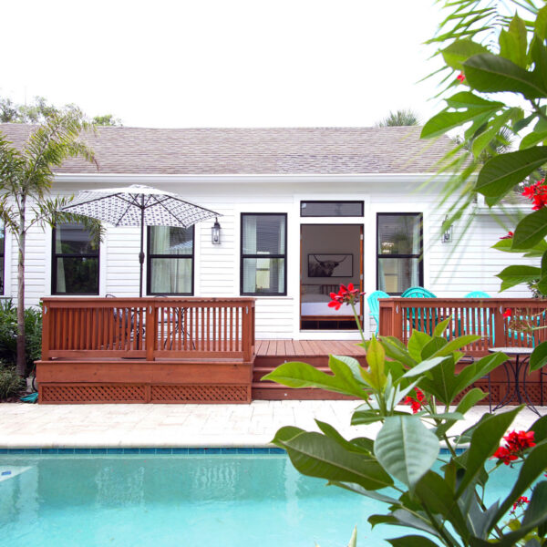 16-shotgun-house-exterior-rear-elevation-pool-view Rear elevation of the white clapboard house seen across the pool with its deck and open bedroom door