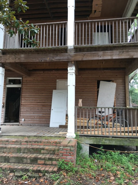 classic-colonial-before-front-porch-removed-doors-jacksonville-mnm-homes-04-02 Before restoration: front porch with a removed panel door and loose materials leaning against the wall
