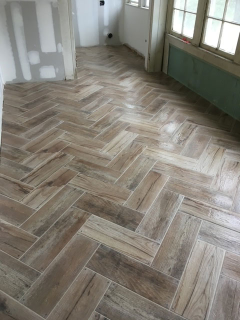 modern-farmhouse-during-completed-herringbone-tile-floor-jacksonville-mnm-homes-07-08 Renovation in progress: completed herringbone wood look tile floor in a room with unfinished drywall walls