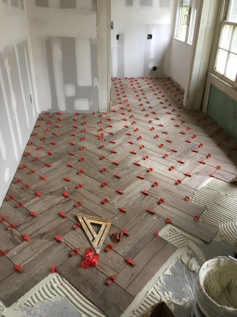modern-farmhouse-during-herringbone-tile-floor-install-jacksonville-mnm-homes-07-07 Renovation in progress: wood look tile being set in a herringbone pattern with red leveling clips in place