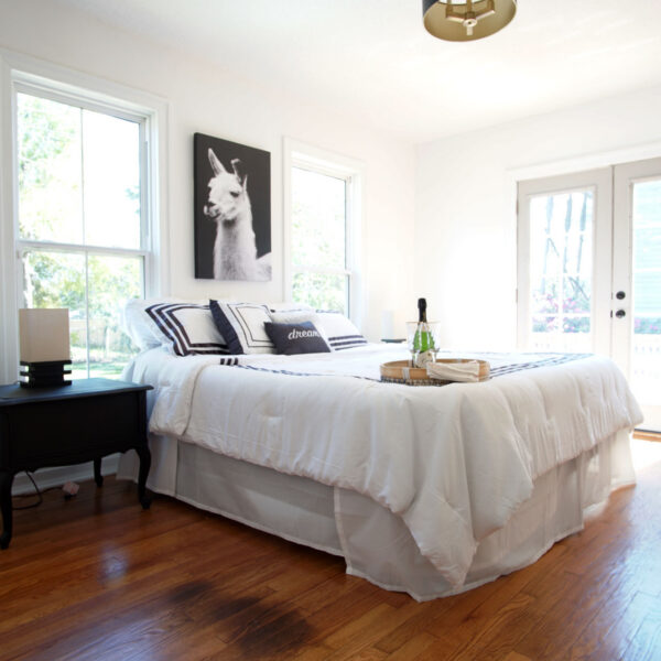 modern-farmhouse-primary-bedroom-jacksonville-mnm-homes-07 Airy bedroom with a made bed hardwood floors and glass doors opening onto the rear deck