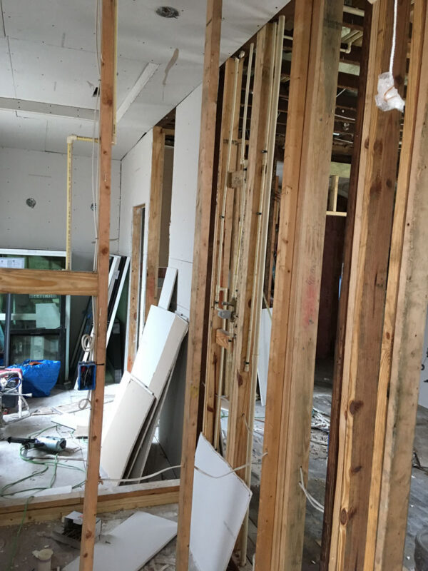shotgun-house-before-partition-framing-drywall-staging-jacksonville-mnm-homes-03-05 Before renovation: stud partitions and exposed piping with drywall sheets stacked nearby