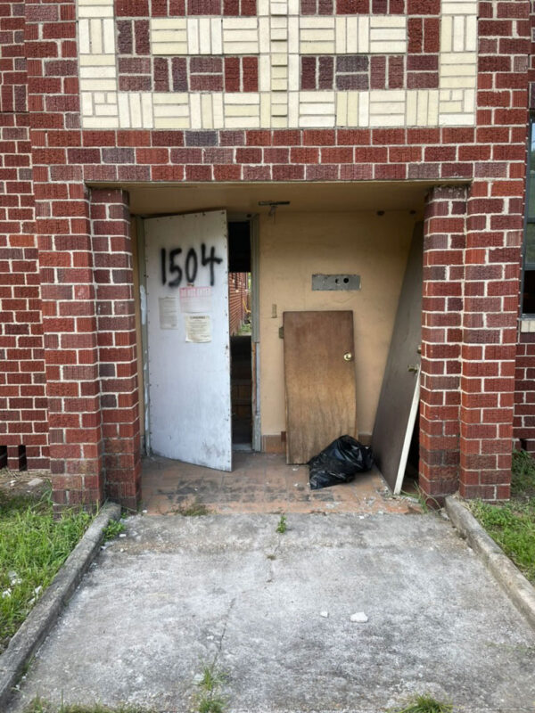 zen-garden-before-weathered-entry-door-brick-facade-jacksonville-mnm-homes-05-01 Before renovation: worn metal entry door and posted notices set in a patterned brick facade