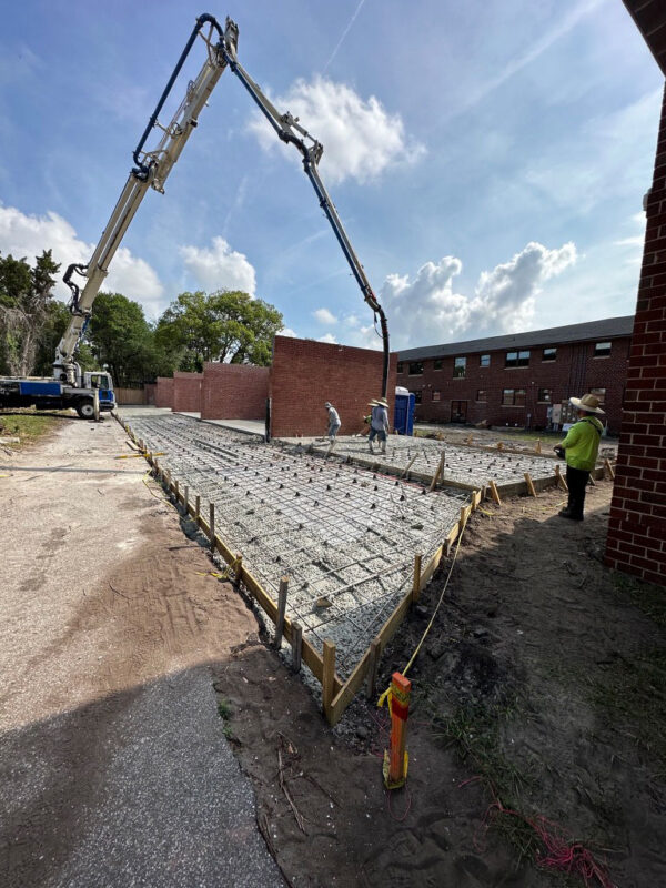 zen-garden-during-reinforced-concrete-slab-pour-jacksonville-mnm-homes-05-15 Work in progress: crew and a concrete pump placing a reinforced slab beside the brick building