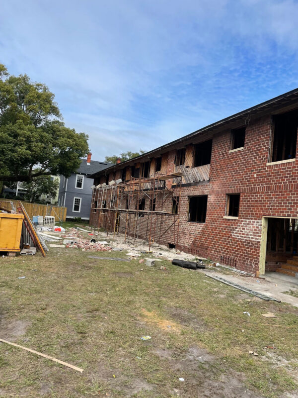 zen-garden-during-scaffolded-brick-facade-repair-jacksonville-mnm-homes-05-14 Work in progress: scaffolding set against a brick exterior with open window bays and a waste dumpster